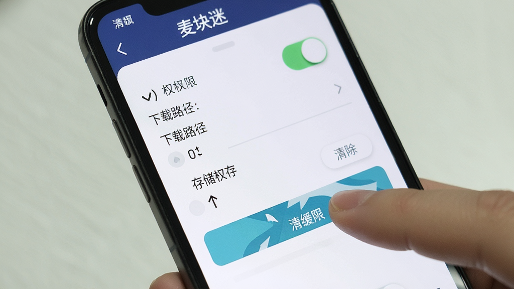 一张展示手机屏幕上麦块迷应用设置界面的图片,界面中包含权限开关、下载路径选择、清除缓存按钮等选项。画面中有一只手指正在点击“存储权限”选项。整体风格为清晰简洁的移动端UI界面,细节丰富,画质干净,无多余元素,界面顶部显示“麦块迷”。