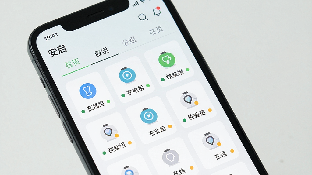 一张展示智能手机界面的图片,画面中“安启”应用显示设备分组管理页面,页面以标签页形式切换不同分组,每个分组下以网格形式排列设备图标,图标下方有设备名称和在线状态小圆点。界面风格清新浅色,排版规整,细节上圆点颜色区分明显,画质干净,无多余元素。