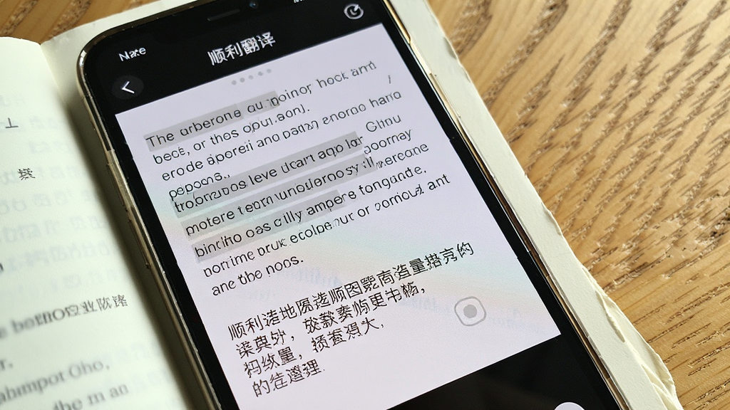 一张手机拍摄书本页面的场景图,手机屏幕上显示“顺利翻译”的拍照翻译界面,原文为英文段落,下方显示中文译文,画面光线自然,背景是木质桌面,风格写实,细节丰富,画质清晰,构图干净