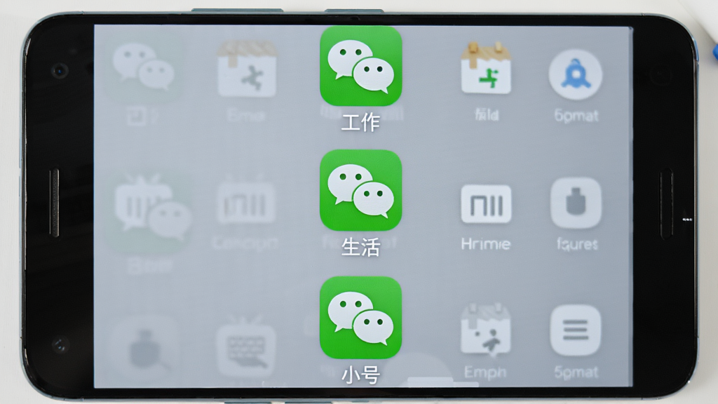 影分身应用多开功能展示图,主体是一台安卓手机,屏幕上同时显示三个微信图标分别标注工作、生活、小号,布局为竖向排列,排版整齐,风格为写实手机界面风格,细节包括图标下方文字标签、背景为浅灰色桌面壁纸,画质清晰干净,无多余元素