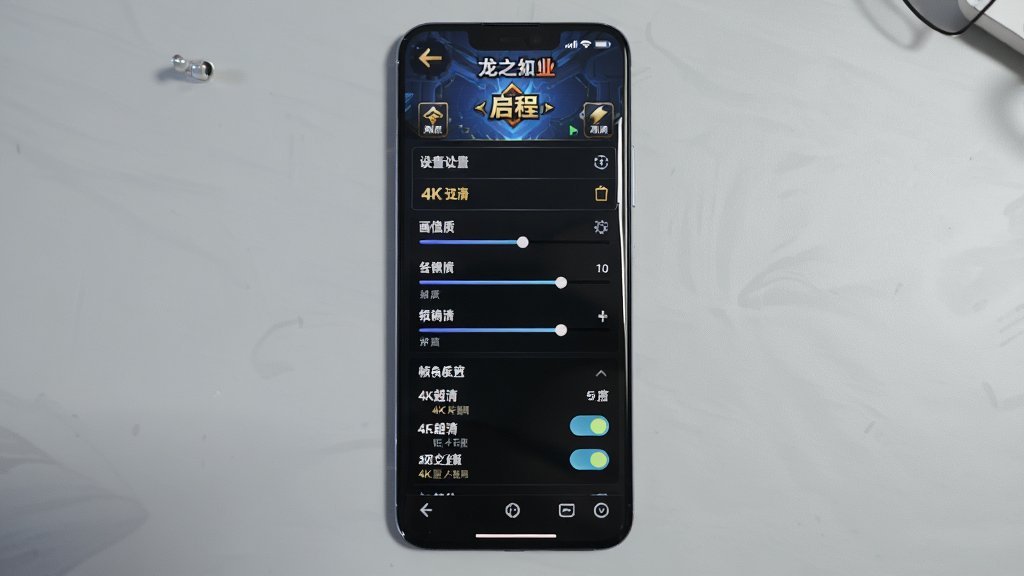 画面主体为一部智能手机屏幕显示龙之谷启程游戏设置界面,布局为手机居中背景为浅灰色桌面,排版采用产品展示风格,风格为简洁科技感,细节包括设置选项列表、画质调节滑块、帧率开关,画质为4K超清、干净、无多余元素,画面中不出现任何文字。