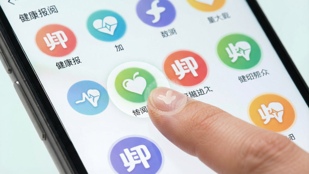 健康报APP频道订阅界面,手机屏幕展示多个彩色圆形图标代表不同健康频道,用户手指正在点击其中一个图标,背景为柔和浅色,风格清新明快,画质细腻,无多余元素