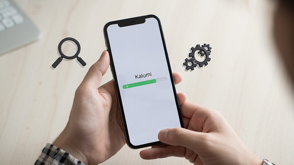 画面为一双手持握手机,手机屏幕显示“Kalumi”安装进度条,旁边有放大镜图标与齿轮图标点缀,背景为浅色桌面环境,风格写实简洁,细节清晰,画质干净,无多余元素