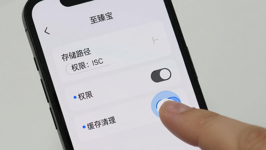 手机屏幕显示“至臻宝”设置页面,包含存储路径选择、权限开关、缓存清理等选项,界面为浅色卡片风格,旁边有手指点击示意,背景简洁,画质清晰,无多余元素