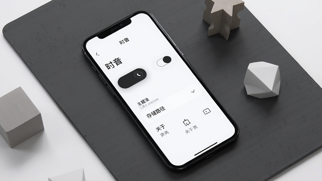 手机屏幕展示“时音”设置界面,界面中有深色与浅色主题切换开关、存储路径选择选项与关于页面入口,手机斜放在深灰色背景板上,旁边散落几个几何形状的装饰块,构图采用对角线构图,风格为极简现代UI展示风格,细节包括屏幕内文字清晰可辨与按钮图标简洁,画质锐利干净,无多余元素