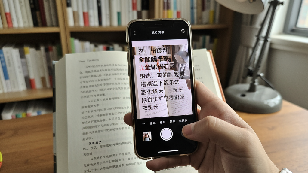一只手手持手机对准一本外文书籍拍照,手机屏幕显示全能翻译家拍照翻译界面,图片中的文字被识别并覆盖显示中文译文,背景为书房环境,风格写实自然,布局突出手机屏幕内容,画质清晰,画面干净