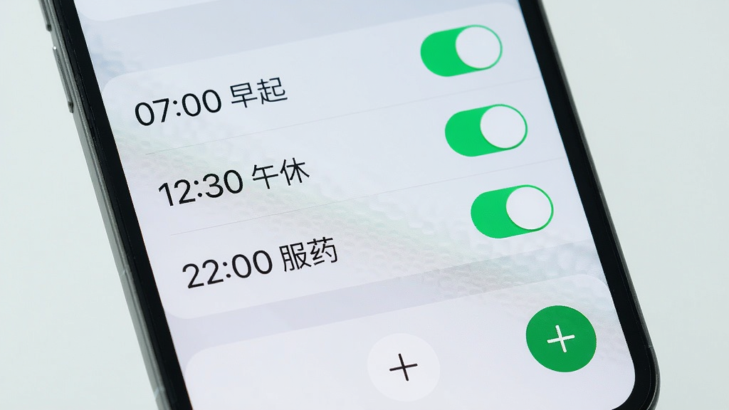 手机屏幕特写展示准点响铃闹钟的闹钟列表页面,列表中有三个闹钟条目分别标注