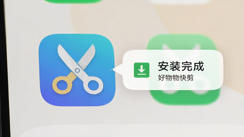手机桌面显示好物快剪应用图标,旁边有安装完成提示气泡,背景为浅色桌面壁纸,风格写实简洁,细节包含应用图标上的剪刀元素与下载完成标识,画质清晰,画面干净,无多余元素