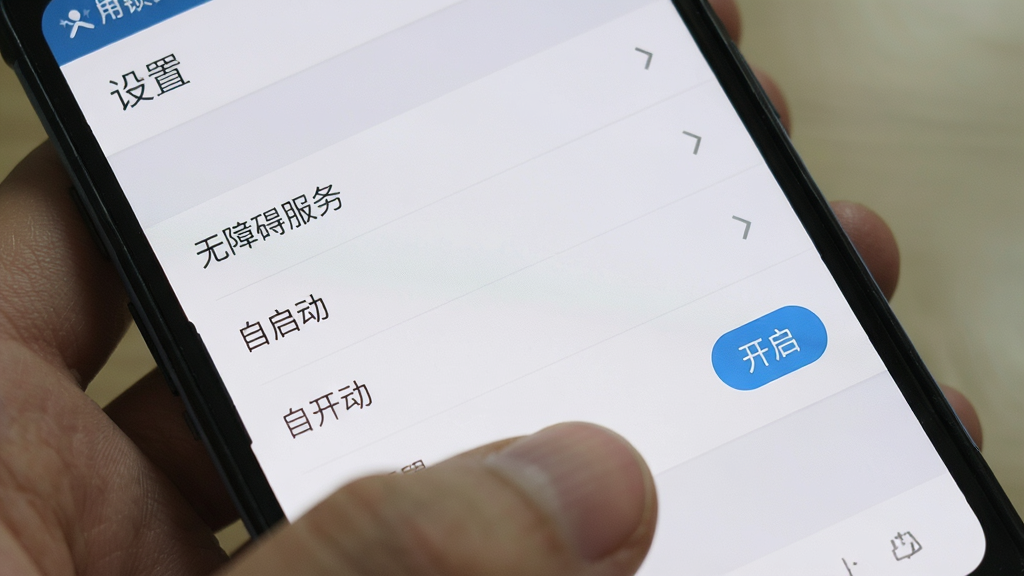 手机应用锁Plus运行在安卓手机上,界面显示“设置”页面,包含“无障碍服务”、“自启动”等选项,用户手指正在点击“开启”按钮,背景为手机系统设置界面,风格写实,色彩自然,画质高清,无多余元素