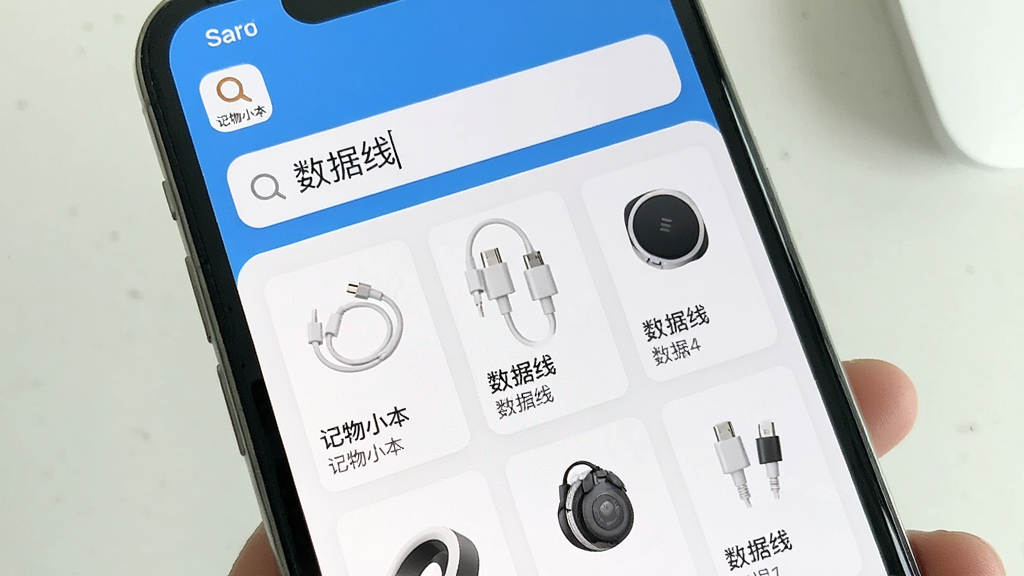 一幅展示记物小本APP智能搜索功能的场景图,主体为手机界面,搜索框中输入“数据线”三个字,下方呈现出多个相关物品卡片,布局为纵向列表,排版简洁明了,风格实用清晰,细节处显示“记物小本”的搜索图标,画质明亮,干净无多余元素。