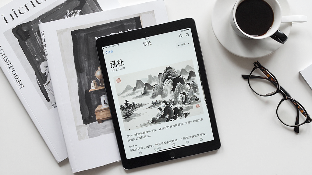 一张俯视角度的摄影图,桌面上散落着艺术期刊与平板电脑,平板中展示“泓社”APP的资讯文章页面,配图是一幅现代水墨画,主体布局错落有致,风格偏向文艺杂志风,细节包含咖啡杯与老花镜,增添生活气息,画质通透自然,干净无多余元素。