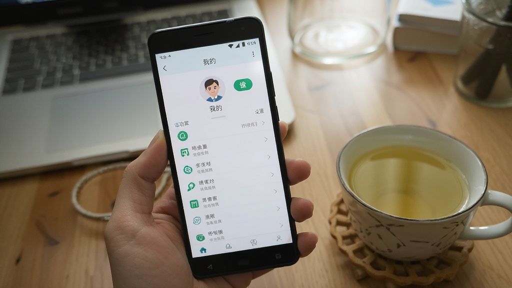 一张展示华诊中医在安卓手机上运行的实拍图,屏幕显示“我的”页面,有个人头像、设置按钮与功能列表,手机旁放着一杯清茶,背景为居家书桌,画面自然明亮,画质干净,无多余元素。