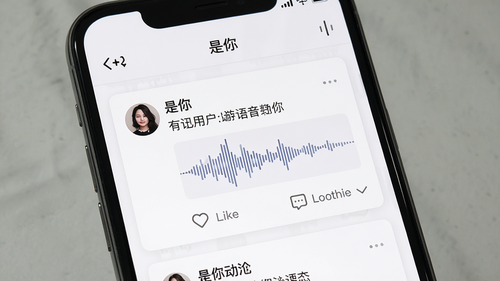 一张展示“是你”软件动态社区页面的手机截图,画面中手机屏幕显示用户发布的语音动态卡片,包含用户头像、文字内容、语音波形图、点赞和评论按钮,界面布局为垂直滚动列表,风格简约清新,背景为白色与浅灰色搭配,细节清晰,画质高清,干净,无多余元素