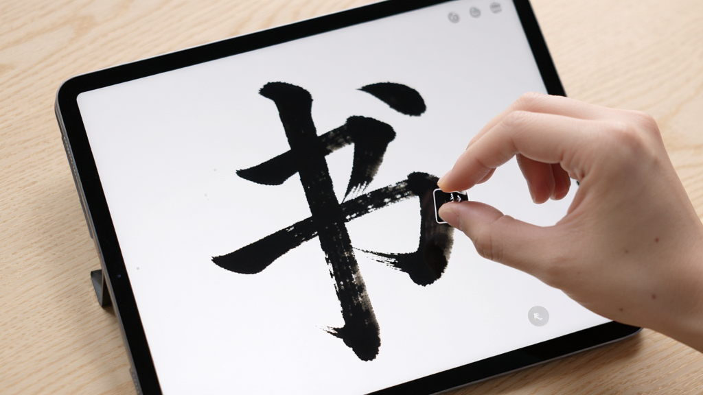 书法数字字库高清放大预览功能,画面展示一部平板电脑,平板屏幕上显示放大后的书法单字,笔画细节清晰可见,屏幕旁边用手指做捏合缩放动作示意,背景为浅色木纹桌面,布局为功能演示图,风格为柔和圆角,细节精致,画质高清,干净无多余元素