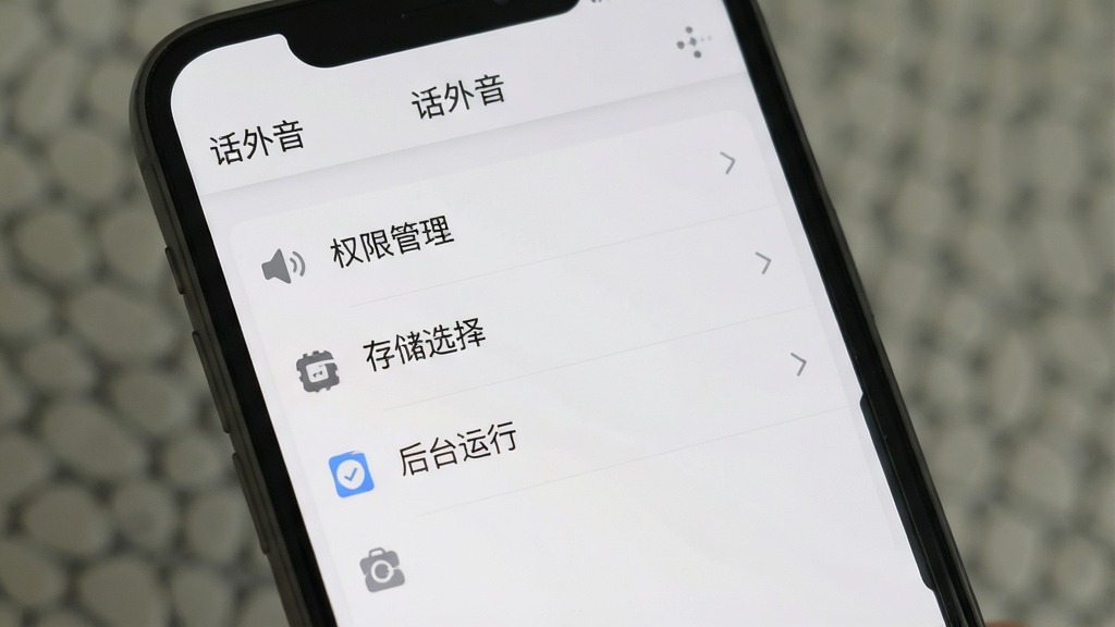 一张展示话外音软件设置界面的图片,手机屏幕上显示权限管理、存储选择、后台运行等选项列表,界面顶部显示“话外音”软件名称,整体采用浅灰色与白色搭配的极简风格,布局清晰,图标简洁,画质干净,无多余元素
