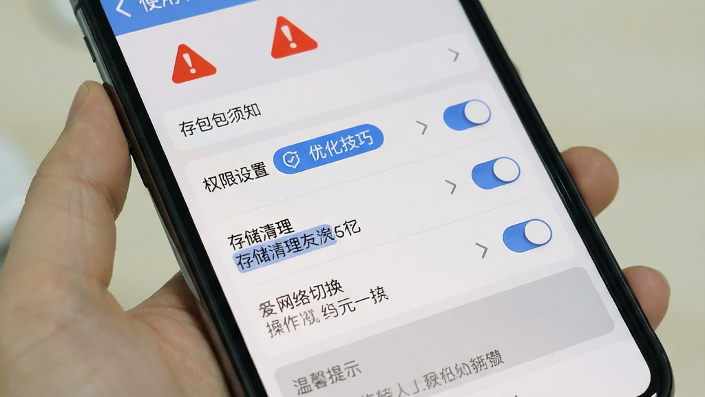 手机屏幕展示“存包包”应用的使用须知页面,画面以列表形式呈现权限设置、存储清理、网络切换等操作提示,顶部有醒目的红色警示图标,中部为蓝色优化技巧标签,底部为灰色温馨提示区域,整体风格为移动端设置界面,细节包括开关按钮、箭头图标、分割线,画质清晰,画面干净,无多余元素