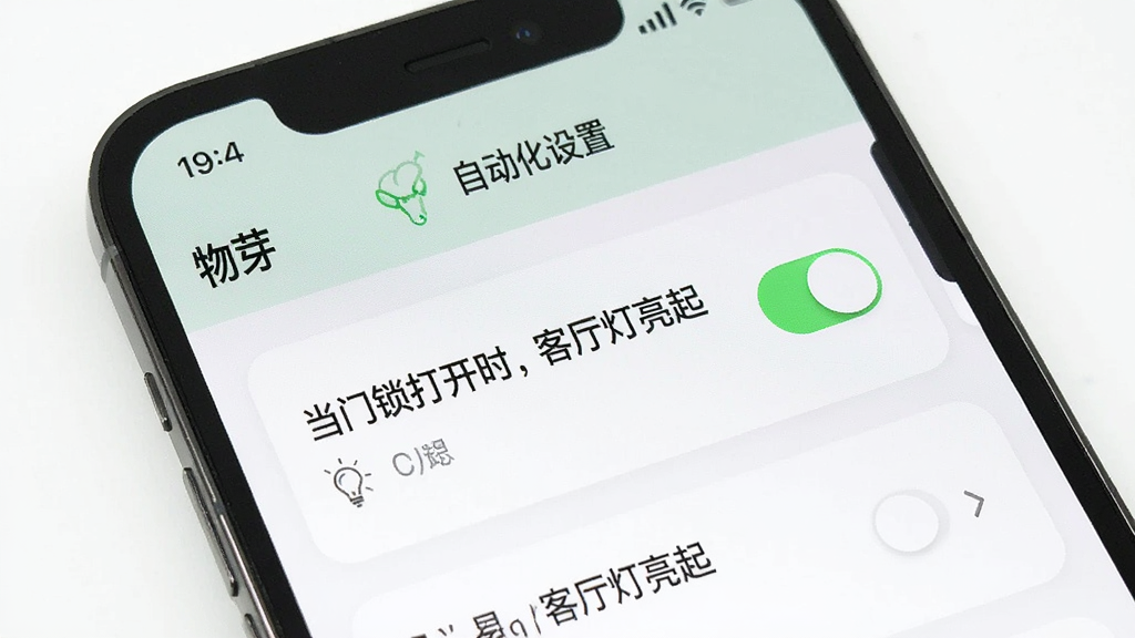 手机屏幕展示“物芽”自动化设置页面,列表中有“当门锁打开时,客厅灯亮起”的规则卡片,旁边有开关按钮;界面清爽,风格现代,细节清晰,画质干净,无多余元素