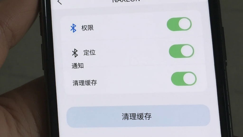 主体为手机屏幕显示NAXEON应用设置页面,布局为上方权限开关列表下方缓存清理按钮,排版纵向清晰,风格为浅色极简,细节包含蓝牙定位通知三个开关项与