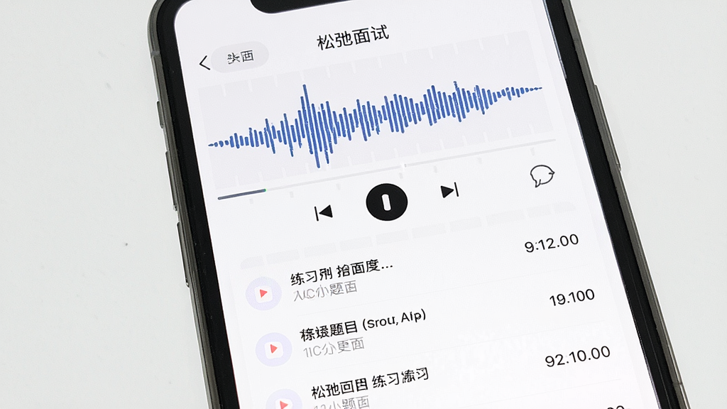 一张展示手机屏幕的图片,屏幕中显示“松弛面试”APP的录音回放界面,界面中有波形图和播放控制按钮,下方列出多条录音记录,每条记录旁边标注着练习题目名称和时长,背景是白色,风格干净利落,画质清晰,无多余元素