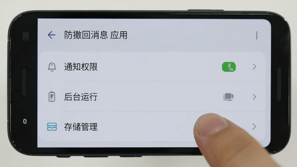一部安卓手机屏幕显示防撤回消息应用设置页面,有“通知权限”“后台运行”“存储管理”等选项,旁边有手指点击操作,背景为浅灰色界面,画质干净,无多余元素
