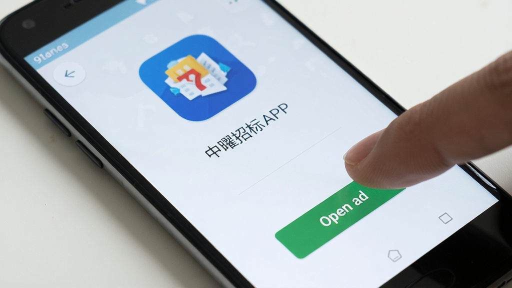 中曜招标APP在安卓手机上的安装完成界面,手机屏幕显示应用图标和打开按钮,背景为浅色桌面,布局为手机正面视图,风格为真实场景展示,细节有手指准备点击打开按钮,画质清晰,干净无多余元素