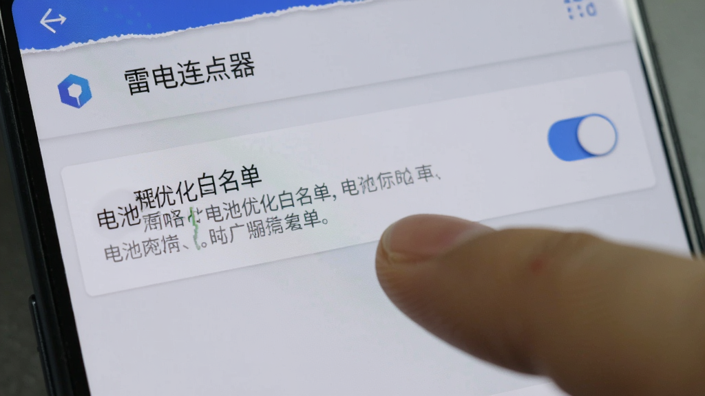 一部安卓手机屏幕显示雷电连点器设置界面,手指正在点击“电池优化白名单”选项,界面有清晰的文字说明和开关按钮,背景为浅灰色,风格简洁实用,细节到位,画质干净无杂物